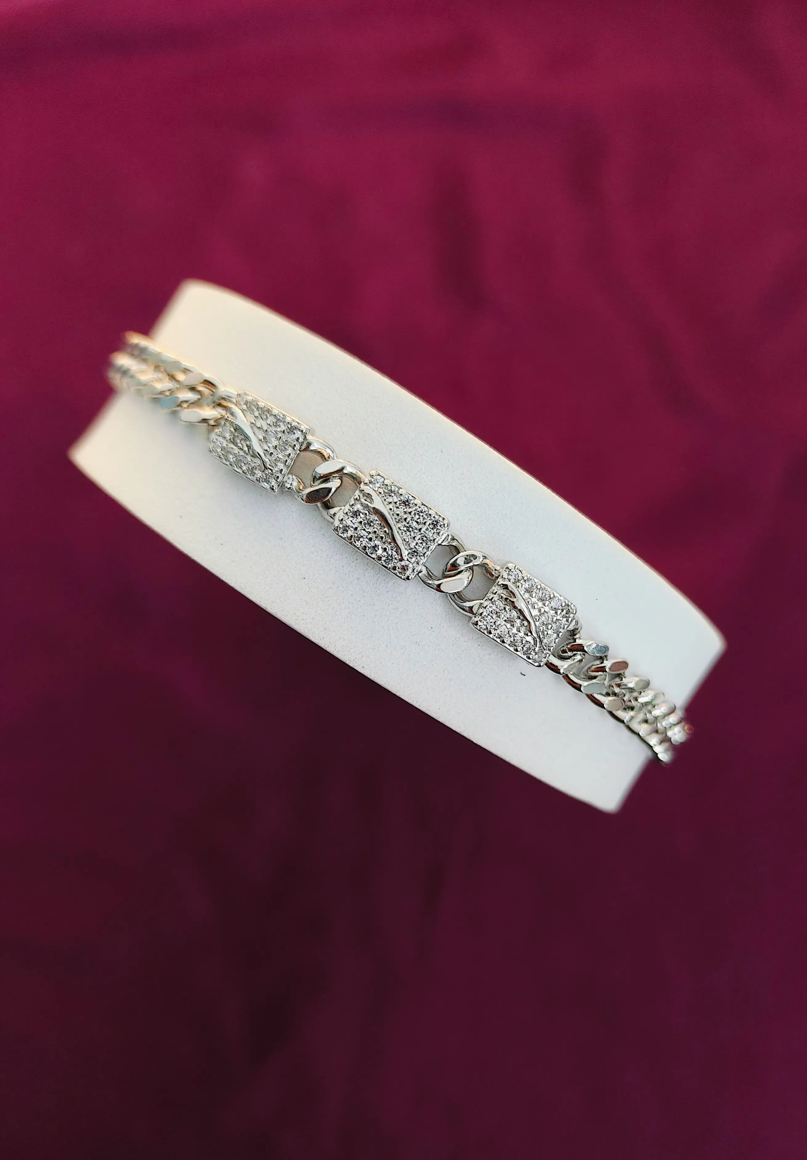 Silver bracelet on a white stand against a purple background